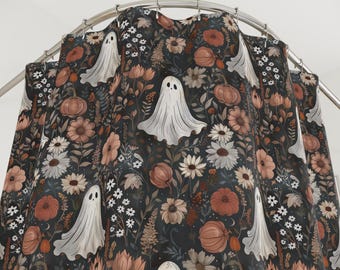 May include: A shower curtain featuring a dark background with a repeating pattern of white ghosts, pumpkins, and various flowers in shades of orange, brown, and white. The curtain is hanging from a curved metal rod.
