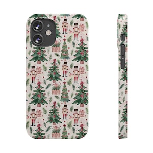 May include: A white phone case with a repeating pattern of Christmas trees, nutcrackers, and wrapped gifts. The trees are green with red bows, and the nutcrackers wear red and black uniforms. The case has a camera cutout and side buttons.