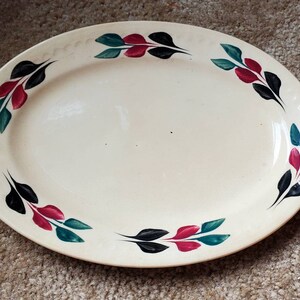 May include: A white oval serving platter with a decorative border of black, red, and green leaves.