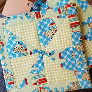 May include: Two green and blue quilted pot holders with a pattern of elephants. The pot holders are made of fabric with a checkered pattern and a blue background with white polka dots.