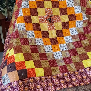 May include: A patchwork quilt with a brown, orange, and yellow checkered pattern. The quilt has a floral border and is made of various fabrics.