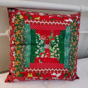 May include: Square decorative pillow with a patchwork design. The pillow features a red background with white polka dots and various Christmas-themed fabric strips in green and red, with gingerbread men and other festive patterns.