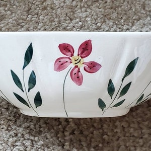May include: White ceramic bowl with a floral design. The bowl features hand-painted red flowers with yellow centers and green leaves. The bowl has a wide, shallow shape, suitable for serving salads or other dishes.