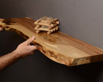 May include: A natural wood shelf with a live edge and a rustic finish. The shelf is mounted to a wall and has a small decorative object on top.