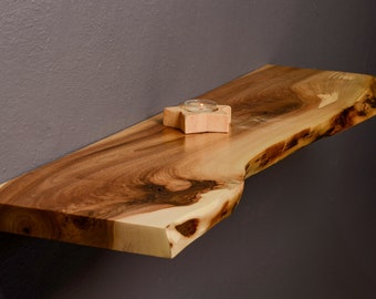 May include: A natural wood shelf with a live edge, stained in a warm brown color. A small wooden candle holder with a lit candle sits on the shelf.
