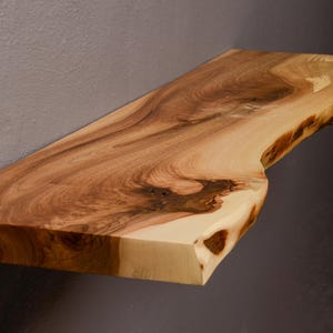 Könnte beinhalten: Ein Regal aus Naturholz mit einer lebenden Kante und einer hellbraunen Farbe. Das Regal besteht aus einem einzigen Stück Holz und hat eine einzigartige, organische Form.