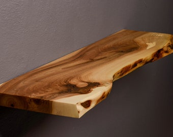 May include: A natural wood shelf with a live edge and a light brown color. The shelf is mounted on a wall.
