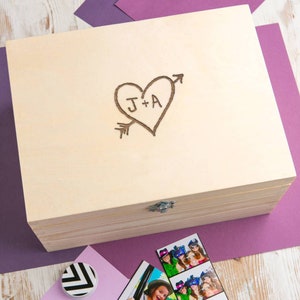 May include: A wooden box with a hinged lid. The lid is engraved with a heart and arrow design and the initials "J+A".