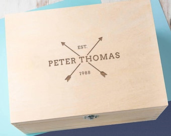 May include: A wooden box with a hinged lid and a latch. The box is engraved with the text "EST. 1988 PETER THOMAS" and two crossed arrows.