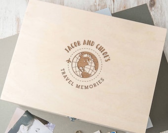 May include: A wooden box with a personalized inscription that reads "Jacob and Chloe's Travel Memories". The inscription features a globe with a plane and a dotted line around it.