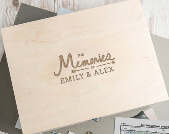 May include: A wooden box with the text "The Memories of Emily & Alex" engraved on the lid. The box is light brown and has a simple design.
