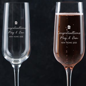 May include: Two champagne flutes with the text "Congratulations May & Dan New Home 2025" etched on them. One flute is filled with pink champagne.