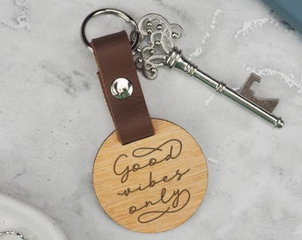 May include: A brown leather keyring with a wooden circle charm that says "Good vibes only". The keyring also has a silver key-shaped bottle opener attached.