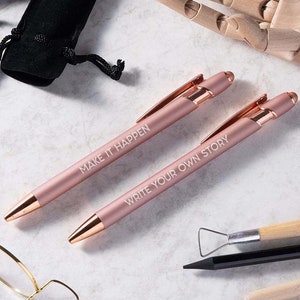 May include: Two rose gold pens with white lettering. The pen on the left says "Make it Happen" and the pen on the right says "Write your own story".