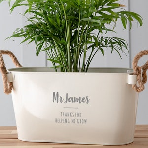 May include: White metal planter with rope handles, featuring the text "Mr. James Thanks for helping me grow". A green plant is growing inside the planter.