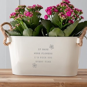 May include: White metal planter with rope handles, featuring the text "If nans were flowers I'd pick you every time". The planter is filled with pink flowers and green foliage.