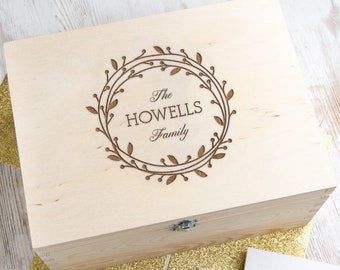 May include: A wooden box with a hinged lid and a latch. The lid is engraved with a wreath design and the text "The Howells Family".