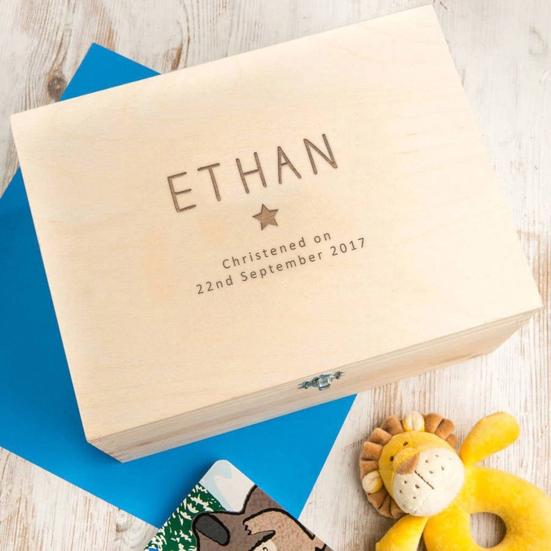 May include: A wooden keepsake box with a light wood finish. The box has an engraved inscription that reads "ETHAN Christened on 22nd September 2017" with a star symbol above the name.