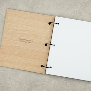 Pode incluir: Um caderno com capa de madeira e uma p&aacute;gina branca aberta. A capa de madeira tem o texto "Your personalised message here." gravado.