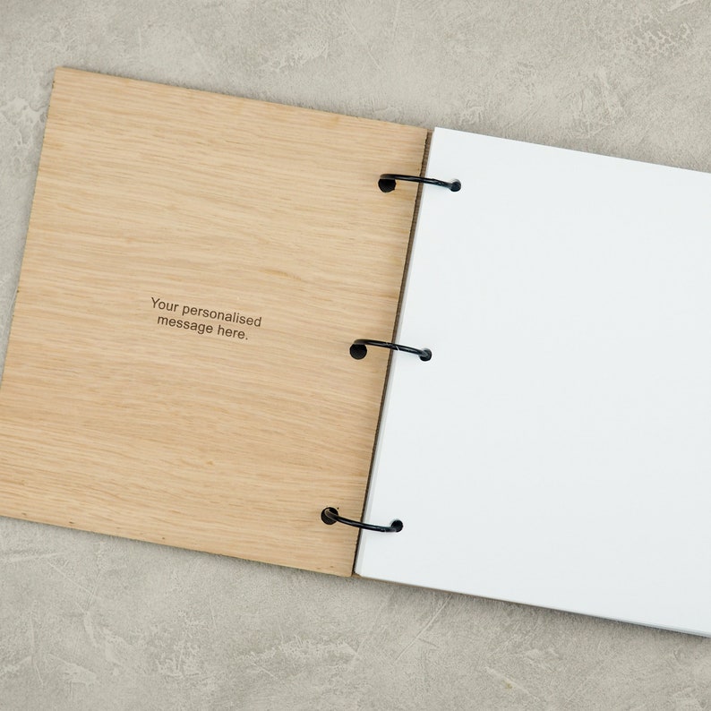 Pode incluir: Um caderno com capa de madeira e uma p&aacute;gina branca aberta. A capa de madeira tem o texto "Your personalised message here." gravado.