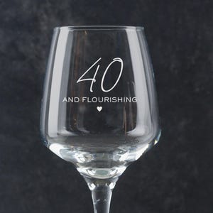 Puede incluir: Una copa de vino de vidrio transparente con el texto "40 and flourishing" grabado en el lateral. El n&uacute;mero 40 est&aacute; escrito en letra cursiva.