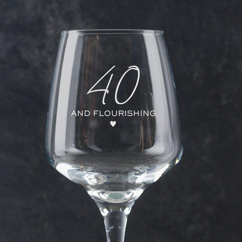 Puede incluir: Una copa de vino de vidrio transparente con el texto "40 and flourishing" grabado en el lateral. El n&uacute;mero 40 est&aacute; escrito en letra cursiva.