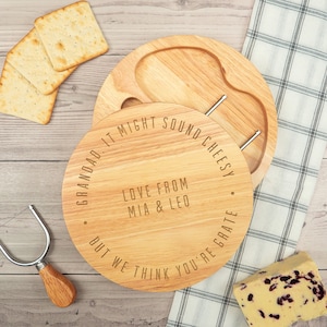 May include: A round wooden cheese board with a built-in knife and a small well for crackers. The board is engraved with the text "Grandad. It might sound cheesy. But we think you're grate. Love from Mia & Leo."