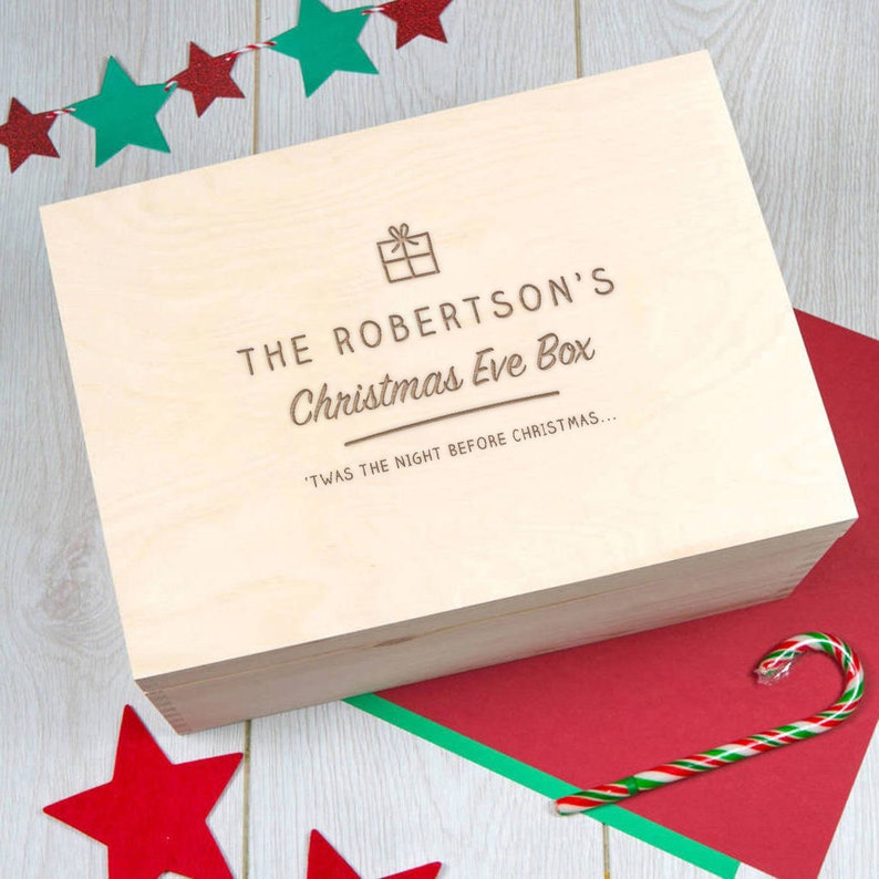 Puede incluir: Una caja de madera con el texto "THE ROBERTSON'S Christmas Eve Box" y "'TWAS THE NIGHT BEFORE CHRISTMAS..." grabado en la tapa. La caja est&aacute; decorada con un peque&ntilde;o icono de regalo.