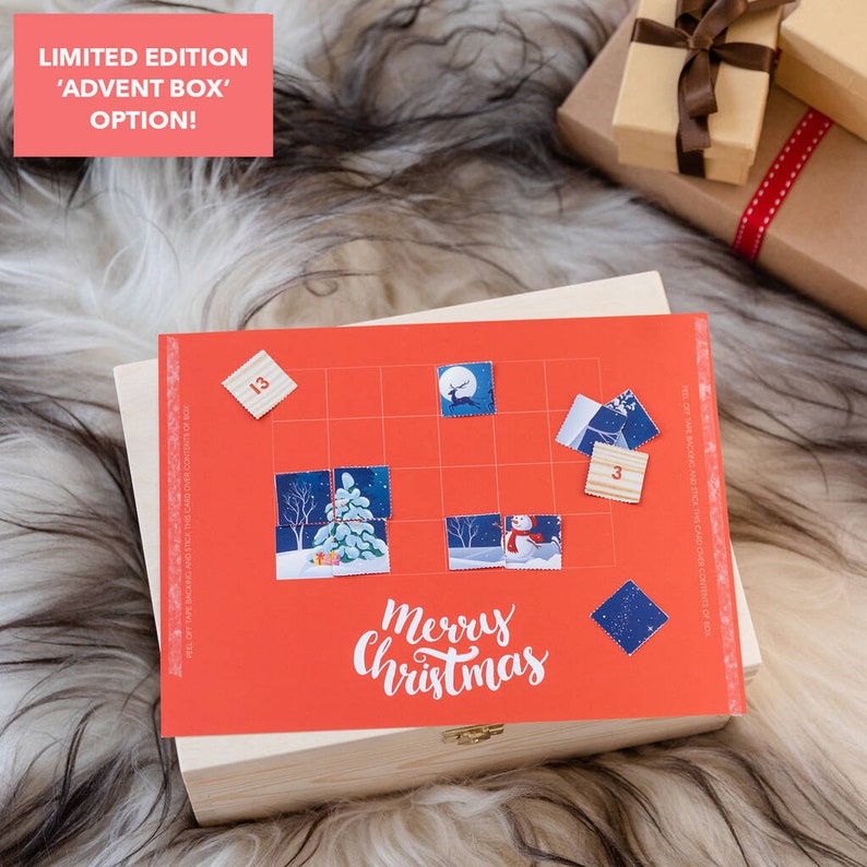 Puede incluir: Una caja de madera roja con un calendario de adviento de tem&aacute;tica navide&ntilde;a en la parte superior. El calendario tiene una cuadr&iacute;cula de cuadrados con n&uacute;meros e im&aacute;genes de un mu&ntilde;eco de nieve, un reno y un &aacute;rbol de Navidad. La caja tiene una tapa con bisagras y un peque&ntilde;o pestillo de metal. El texto "Feliz Navidad" est&aacute; impreso en el calendario.