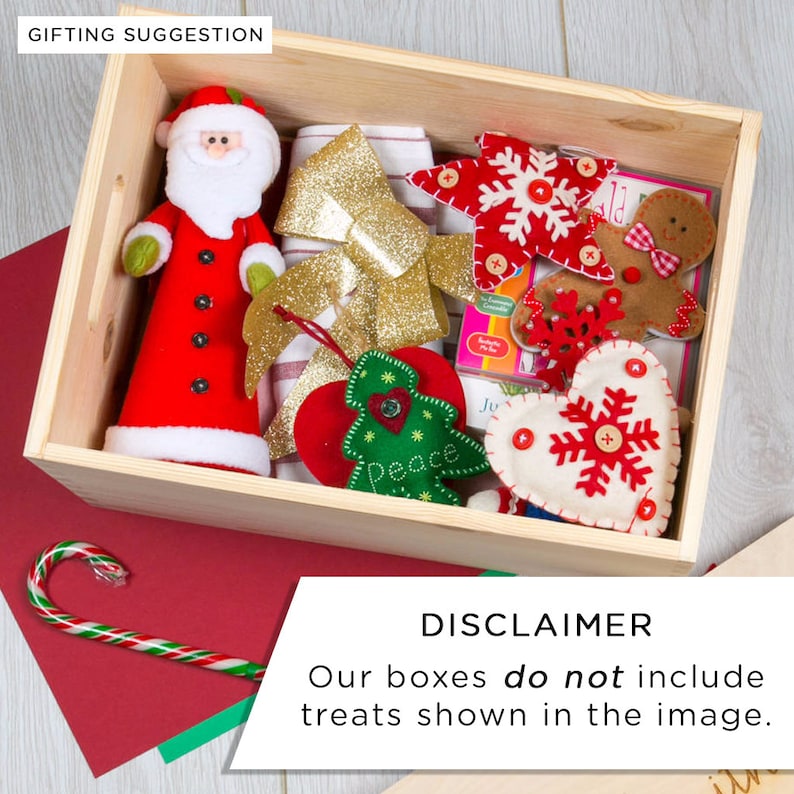 Puede incluir: Una caja de madera llena de adornos navide&ntilde;os de fieltro, incluyendo un Pap&aacute; Noel, una estrella, un hombre de jengibre, un coraz&oacute;n y un &aacute;rbol de Navidad. La caja est&aacute; sobre una superficie a rayas rojas y verdes. "AVISO: Nuestras cajas no incluyen las golosinas que se muestran en la imagen." est&aacute; escrito en una superficie roja.
