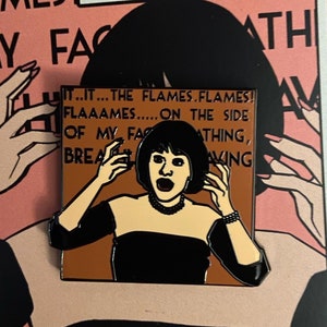 May include: A black and white enamel pin featuring a woman with black hair and a black dress. The pin is set against a pink background with the text "FLAMES" in white. The text "IT...IT... THE FLAMES. FLAMES! FLAAAMES..... ON THE SIDE OF MY FACE...ATHING, BREATH...AVING" is also visible on the pin.