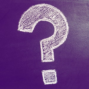 May include: A white chalk question mark on a dark purple background. The question mark is hand-drawn with visible texture, suggesting a chalkboard or similar surface. The image is a simple, yet striking visual.