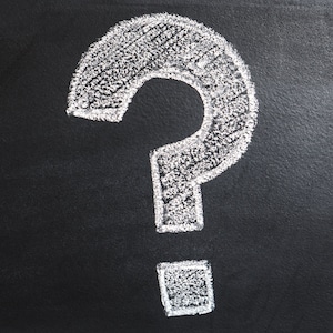 May include: A white question mark drawn in chalk on a black chalkboard.