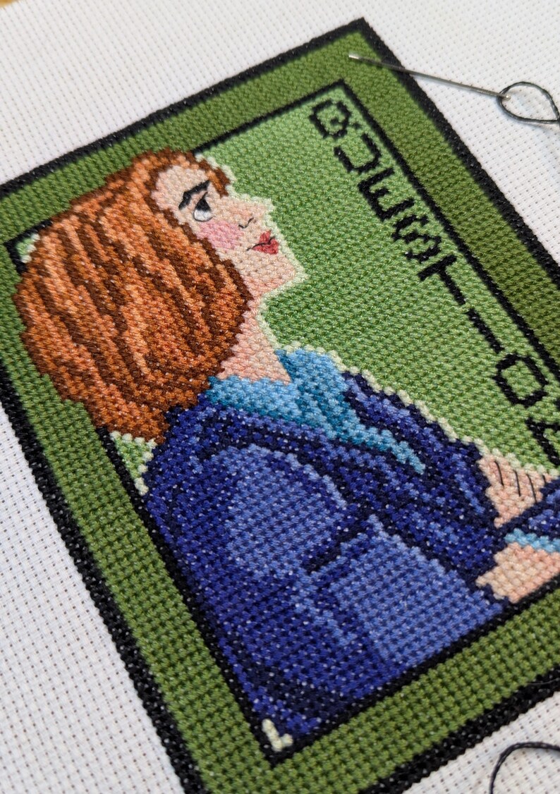 May include: Cross-stitch embroidery of a woman with brown hair wearing a blue jacket. The background is green with the text "COUNT-DOWN" in black.
