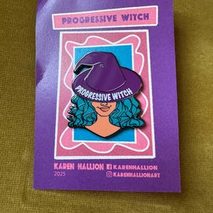May include: A purple enamel pin featuring a witch with teal hair and a purple witch hat. The pin has the words "Progressive Witch" on the hat and the card. The card is purple with the artist's name and social media handles.