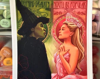 May include: A rectangular art print featuring two figures in profile. On the left, a green-skinned figure in a black witch hat and cloak with the text "DEFYING GRAVITY". On the right, a blonde figure in a pink gown and crown with the text "YOU'LL BE POPULAR".