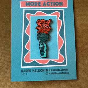 May include: A teal card with a pin featuring a torch with the text "LESS OUTRAGE MORE ACTION". The card has the text "MORE ACTION" at the top and the artist's name and social media handles at the bottom.