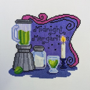 May include: Cross-stitch design featuring a blender, salt shaker, margarita glass, and a lit candle. The text "Midnight Margaritas" is displayed on a purple background with pink accents. A lime is in the lower left corner.