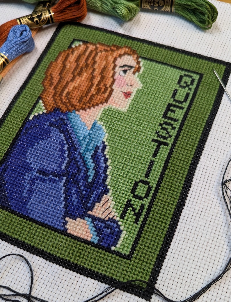 May include: Cross stitch pattern of a woman with brown hair wearing a blue jacket. The background is green and the text "GUEST LIST" is stitched in black.