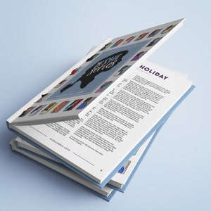 May include: A stack of three blue and white paperback books with the title "The She Series" on the cover. The text "HOLIDAY" is visible on the top page of the book. The book is about a woman named Holiday.