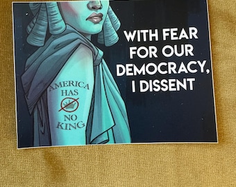 May include: A rectangular sticker with a teal illustration of a person with a powdered wig and a draped garment. The person has a tattoo that says "AMERICA HAS NO KING" with a line through the crown. The sticker has the text "WITH FEAR FOR OUR DEMOCRACY, I DISSENT".