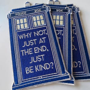 May include: Three rectangular blue embroidered patches shaped like a police box. Each patch features white text that reads: POLICE BOX, WHY NOT, JUST AT THE END, JUST BE KIND? The design includes light yellow window panes and a white border outline.