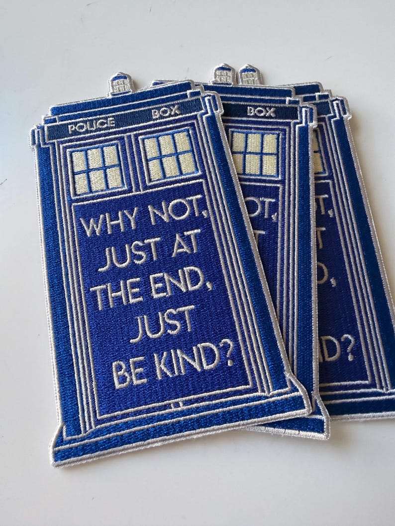 May include: Three rectangular blue embroidered patches shaped like a police box. Each patch features white text that reads: POLICE BOX, WHY NOT, JUST AT THE END, JUST BE KIND? The design includes light yellow window panes and a white border outline.