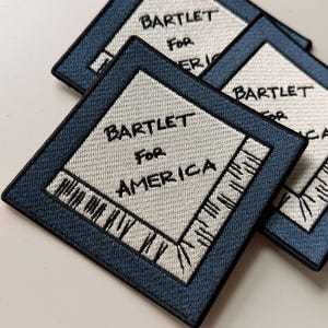 May include: Two square embroidered patches featuring a blue border and a cream-colored center. The text BARTLET FOR AMERICA is stitched in black thread in the center, with black stitched details resembling a floppy disk design on the corners.