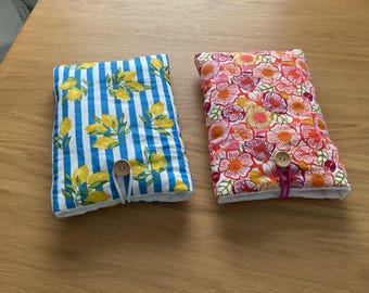 Puede incluir: Dos fundas rectangulares de tela. Una presenta un patrón de rayas azules y blancas con limones amarillos y hojas verdes. La otra tiene un estampado floral en tonos rosas, naranjas y blancos. Cada funda tiene un cierre de botón de madera.
