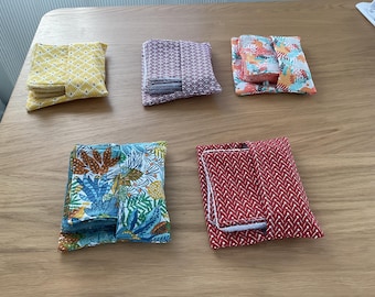 May include: Five different fabric pouches with various patterns. The pouches are folded and stacked on a wooden surface. The patterns include floral, geometric, and abstract designs. The pouches are made of cotton fabric and are perfect for storing small items.