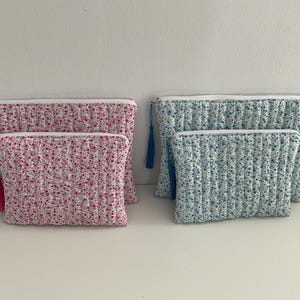 Peut inclure: Quatre trousses de maquillage matelassées en deux tailles. Deux sont roses avec un motif floral et des pompons rouges. Les deux autres sont bleues avec un motif floral et des pompons bleus. Chaque trousse a une fermeture éclair blanche.