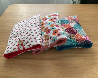 Puede incluir: Cuatro bolsas de tela con diferentes patrones, cada una con un cierre de botón de madera. Las bolsas están apiladas una encima de la otra. Los patrones incluyen cerezas rojas sobre un fondo blanco, flores rosas y blancas y un diseño de hojas tropicales.