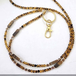 May include: A brown and gold beaded lanyard with a gold clasp and a gold ring. The lanyard has tiger's eye stones and clear crystals.