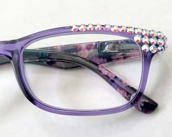 May include: Purple glasses with a floral pattern on the arms and a row of iridescent rhinestones on the top of the frame.